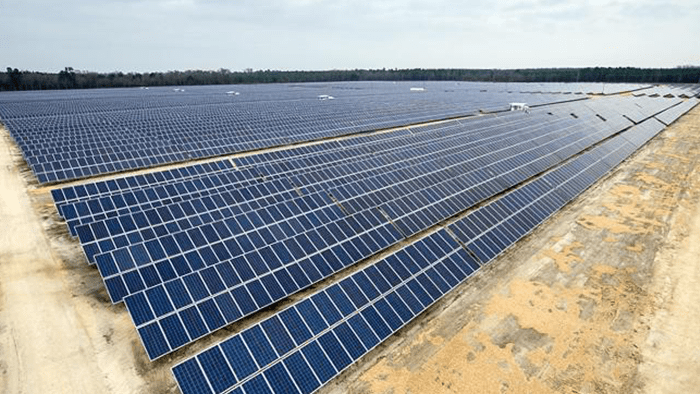  Aerial view of large solar installation on green hills with mountains in background